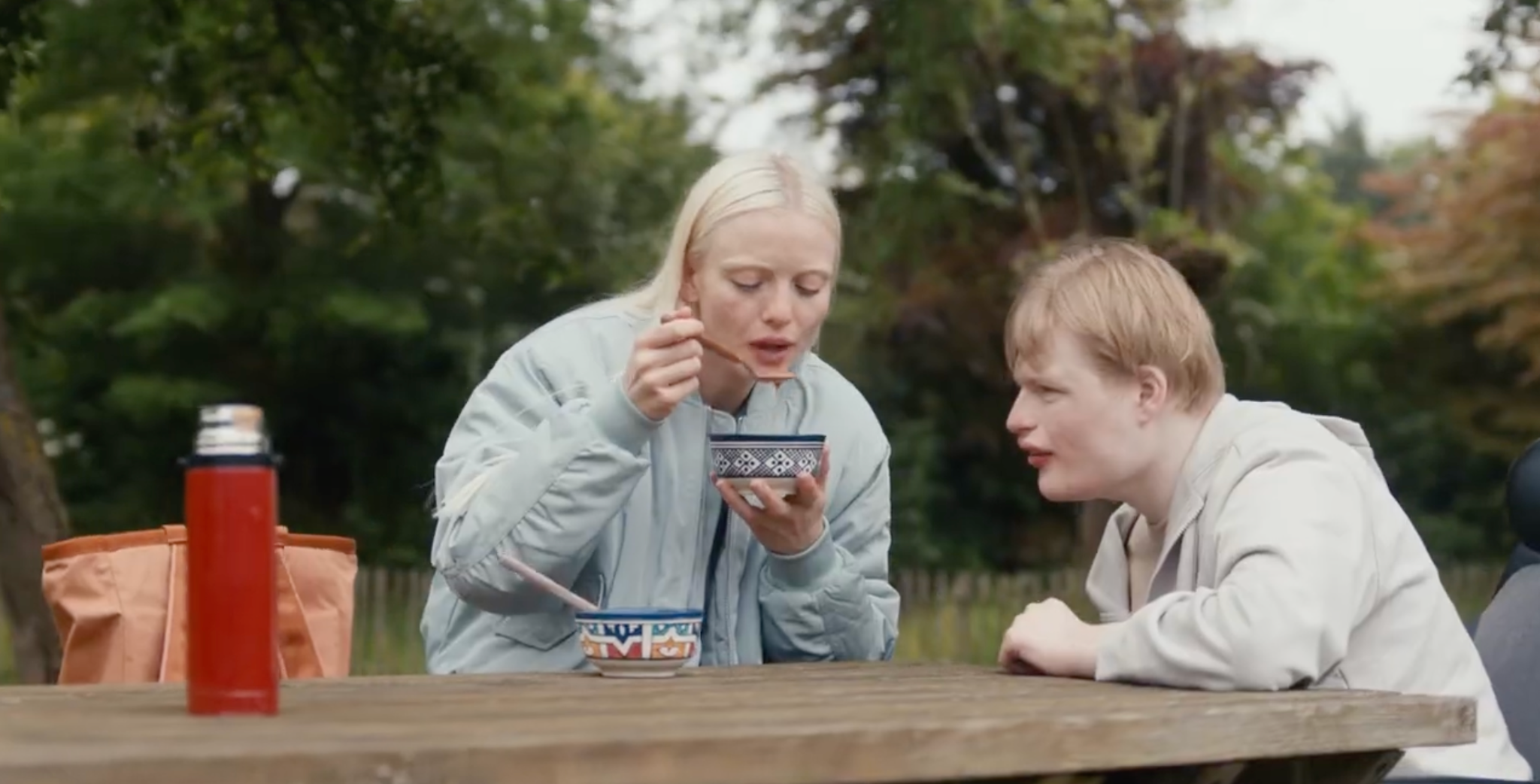 Twee jongeren eten samen soep aan een picknicktafel